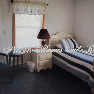 A cozy bedroom featuring a single bed with striped bedding, a nightstand with a lamp, and a window with a curtain.