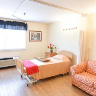 A clean and well-organized hospital room with a bed, chair, and natural lighting.