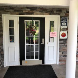 A building entrance with glass double doors, framed in white and set against a brick wall.