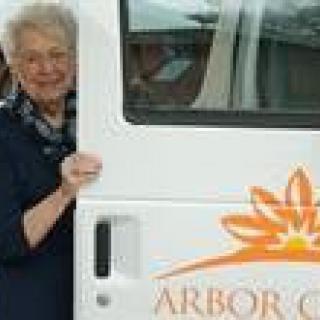 An elderly woman standing next to a van with the logo 'Arbor'.