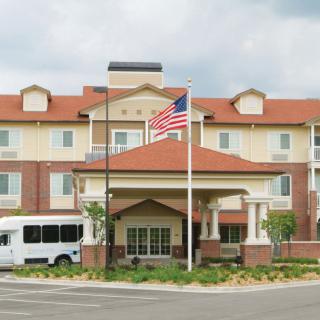 A hotel building with an American flag and a shuttle bus parked in front.