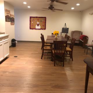 A cozy dining room with a wooden floor, featuring a dining table and chairs, lit by ceiling lights and a ceiling fan.