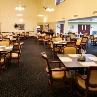 An empty dining area with neatly arranged tables and chairs, carpeted flooring, and soft lighting.
