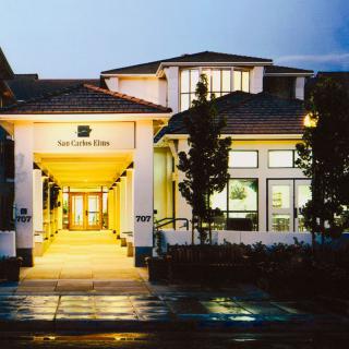 A well-lit building entrance at dusk with surrounding trees and architectural details.