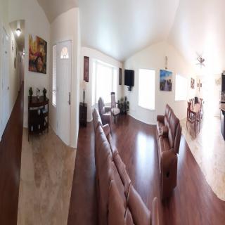 A spacious living room with sofas and a television, featuring wood flooring and an adjacent dining area.
