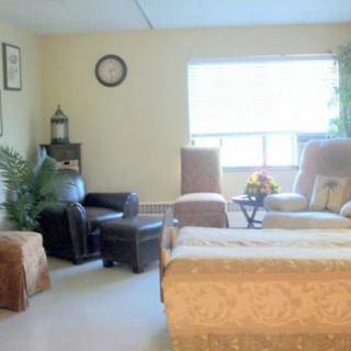 A cozy living room with comfortable seating, a window providing natural light, and decorative elements such as a clock and plants.