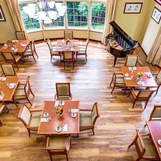 Aerial view of a dining room with neatly arranged tables and chairs, featuring a grand piano by the window.