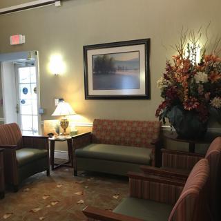 A cozy waiting room with comfortable seating, a decorative painting, and a floral arrangement.