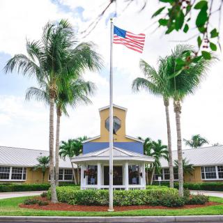 A building entrance surrounded by palm trees with an American flag on a flagpole.
