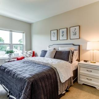 A cozy bedroom with a neatly made bed, soft lighting, and decorative artwork on the wall.