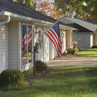 A suburban house with an American flag displayed, surrounded by autumn trees.
