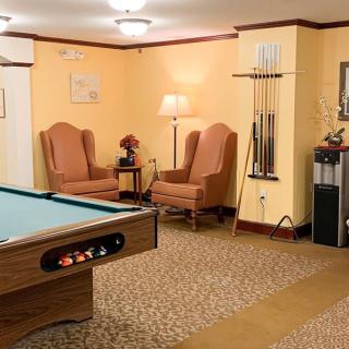A cozy game room featuring a pool table, armchairs, and cue sticks neatly arranged by the wall.