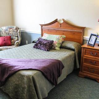 A cozy bedroom with a wooden headboard bed, decorative pillows, and an armchair in the corner.