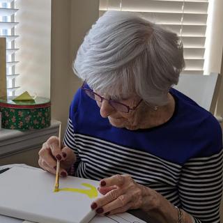 An elderly woman focuses intently on her painting, showcasing her artistic talent.