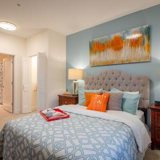 A cozy bedroom with a stylish bed adorned with colorful pillows and modern artwork on the wall.