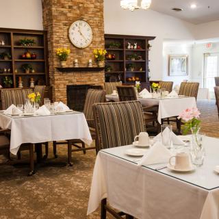 An elegantly decorated dining room with neatly set tables and a cozy brick fireplace.
