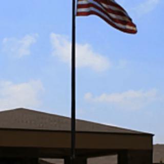 An American flag waving in the breeze above a building under a clear blue sky.