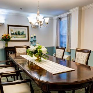 An elegantly decorated dining room with a central table, surrounded by chairs and adorned with a floral centerpiece under a chandelier.
