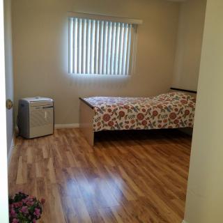 A minimalist bedroom featuring a single bed with floral bedding, wooden flooring, and a window with vertical blinds.