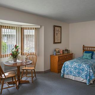 A cozy bedroom with a single bed, a small dining table, and wooden furniture.