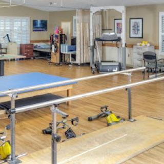 A well-equipped rehabilitation gym featuring various exercise equipment, including a treadmill and parallel bars, designed for physical therapy sessions.