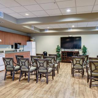A well-equipped conference room featuring a kitchenette, arranged chairs, and a large television.