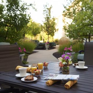 A beautifully set outdoor breakfast table on a sunny patio among lush greenery.