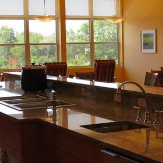 A spacious kitchen with a large countertop and dining area, featuring ample natural light from the surrounding windows.