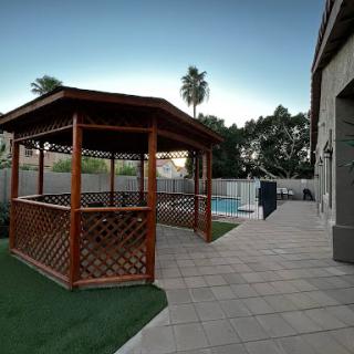 A wooden gazebo beside a pool in a beautifully landscaped backyard.