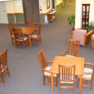 A spacious lounge area with wooden tables and chairs arranged on a carpeted floor.