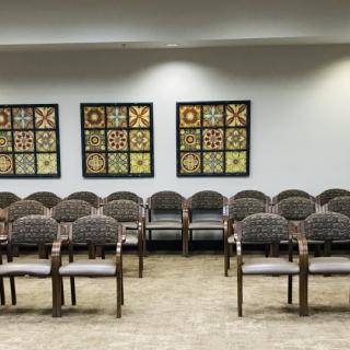 A waiting room with multiple rows of chairs and quilt pattern artwork on the wall.