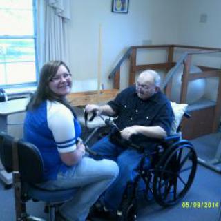A caregiver and an elderly person share a joyful moment indoors.