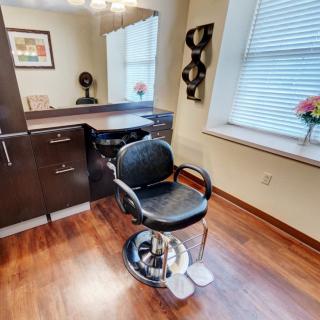 A cozy hair salon setup featuring a styling chair, mirror, and wooden flooring.