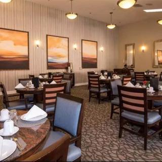 A cozy dining area with neatly arranged tables and chairs, complemented by warm lighting and decorative artwork on the walls.