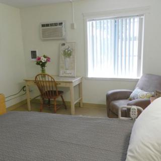 A cozy bedroom with a bed, desk, and chair next to a window with blinds.