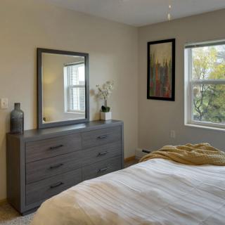 A cozy bedroom featuring a dresser with a mirror, decorated with plants and artwork.