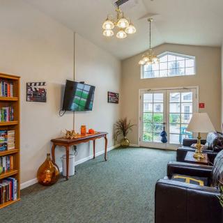 A cozy living room with a television, bookshelf, and large windows.