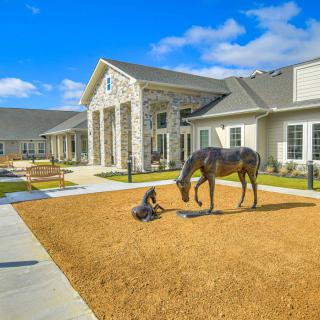 A modern building with a horse sculpture in the front yard under a clear, sunny sky.