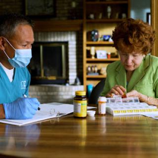 A healthcare professional assists an elderly woman with her medication management at home.