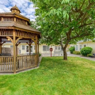 A wooden gazebo in a lush garden with a large tree and well-maintained lawn.
