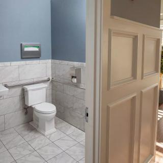 A modern bathroom with a white tiled floor and blue walls, featuring a toilet and an open door.