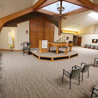 A peaceful chapel interior with seating arranged facing the altar and a prominent cross hanging from the ceiling.
