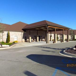 A large building with a covered entrance and a driveway, set against a clear blue sky.