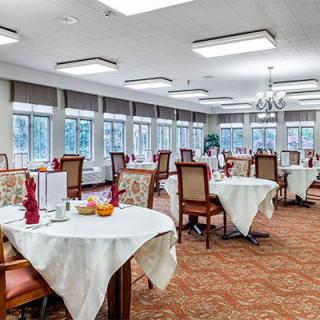An elegantly set dining room with tables and chairs arranged neatly, featuring large windows allowing natural light.