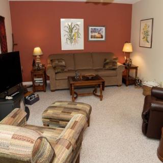 A cozy living room with a sofa, armchairs, and a television, decorated with wall art and lamps.