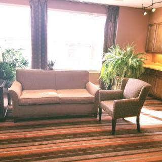A cozy living room setup featuring a couch and an armchair, complemented by plants and abundant natural light.