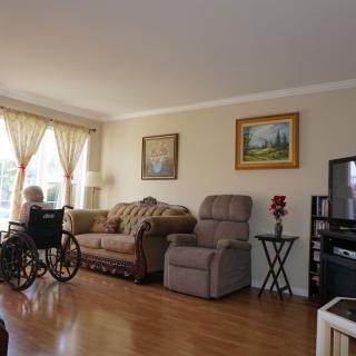 A cozy living room with a wheelchair next to a sofa and armchair, featuring a television and decorative paintings.
