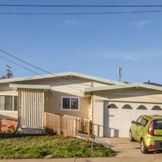 A suburban house with a car parked in the driveway under a clear sky.