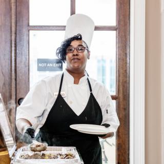 A chef in uniform carrying a plate of food.