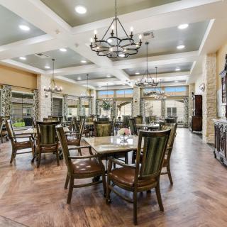 A spacious dining area featuring wooden floors, elegant chandeliers, and neatly arranged tables and chairs.